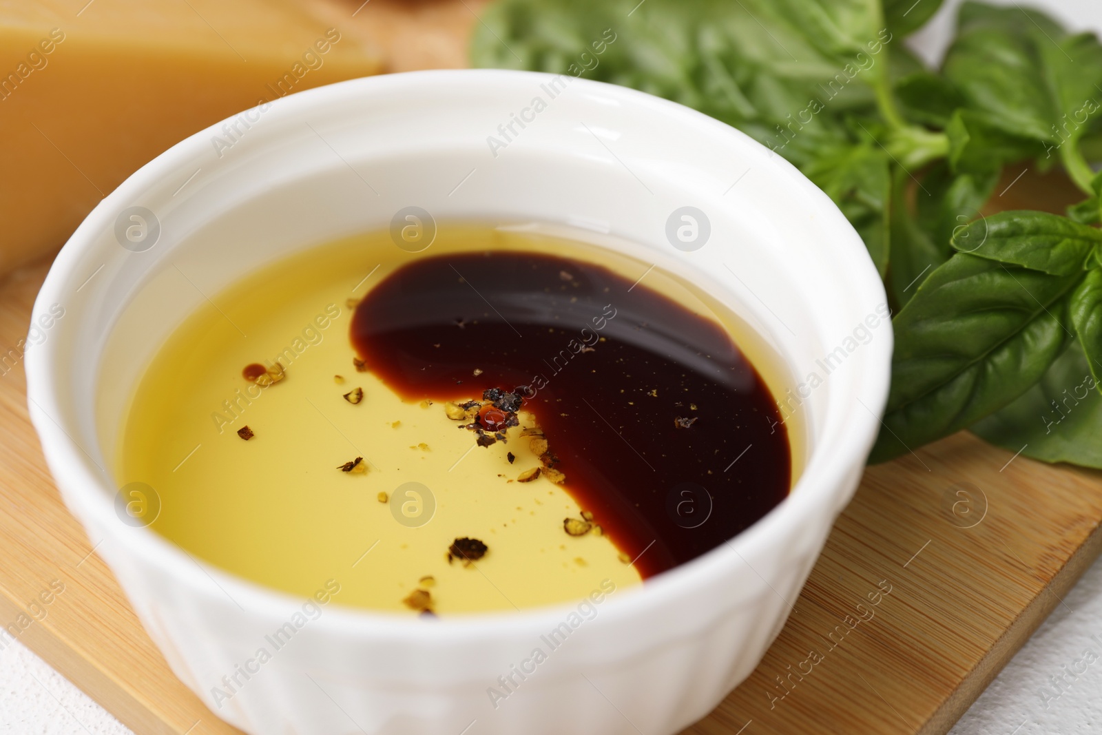 Photo of Bowl of organic balsamic vinegar with oil, spices and basil on table, closeup