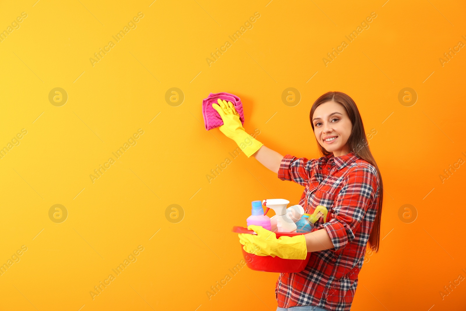 Photo of Young woman cleaning color wall with rag