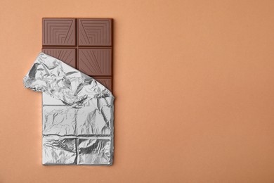 Photo of Tasty chocolate bar on brown background, top view. Space for text