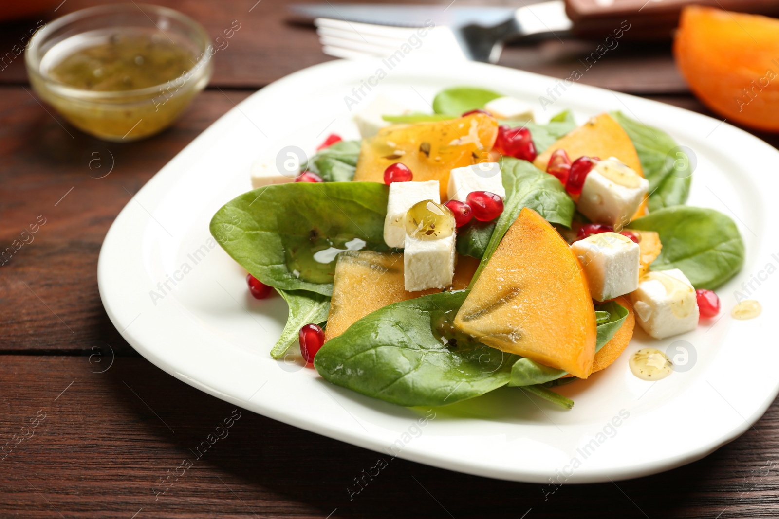 Photo of Delicious persimmon salad with pomegranate and spinach on wooden table, closeup
