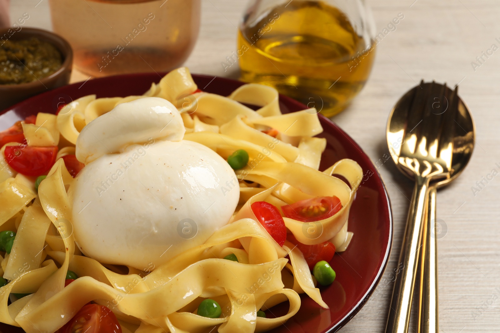 Photo of Plate of delicious pasta with burrata, peas and tomatoes on white wooden table, closeup