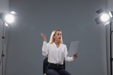 Casting call. Emotional woman with script performing against grey background in studio