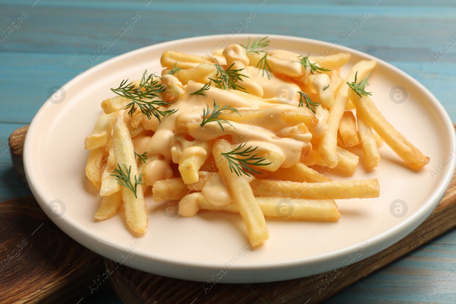 Photo of Delicious french fries with cheese sauce and dill on light blue wooden table, closeup