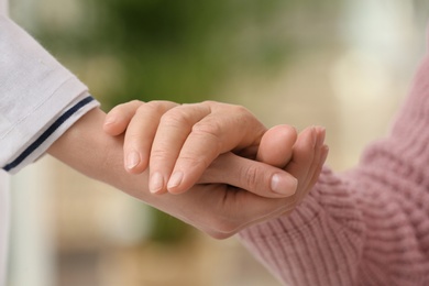 Photo of Nurse holding hand of elderly woman against blurred background, closeup. Assisting senior generation