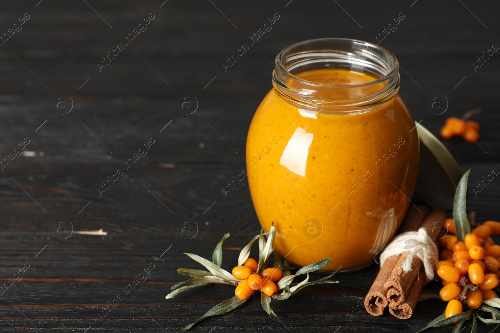 Photo of Delicious sea buckthorn jam and fresh berries on black wooden table. Space for text