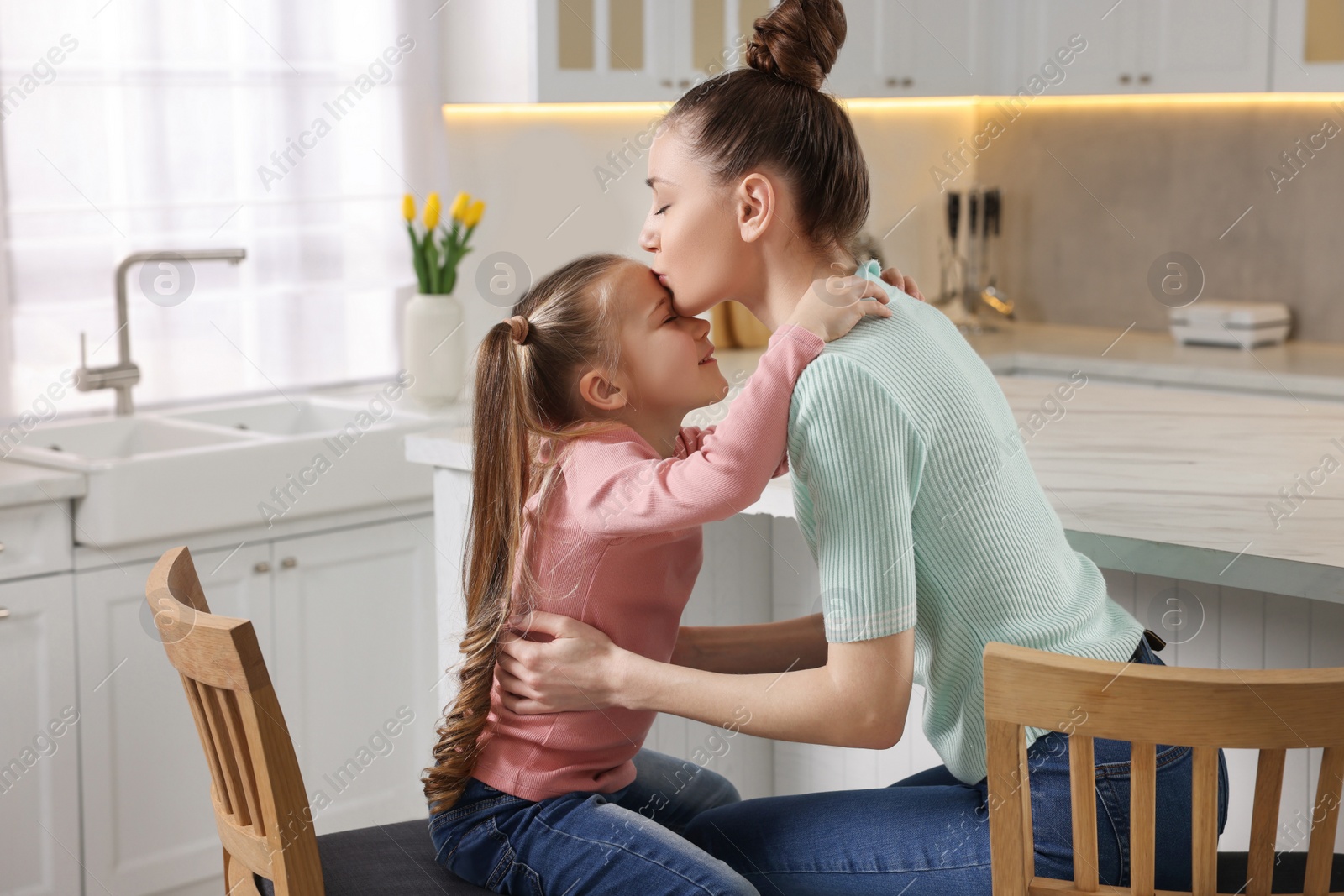 Photo of Happy mother kissing her cute daughter in kitchen