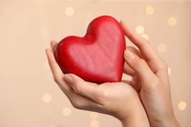 Photo of Woman holding red heart on beige background with festive lights, closeup. St. Valentine's day