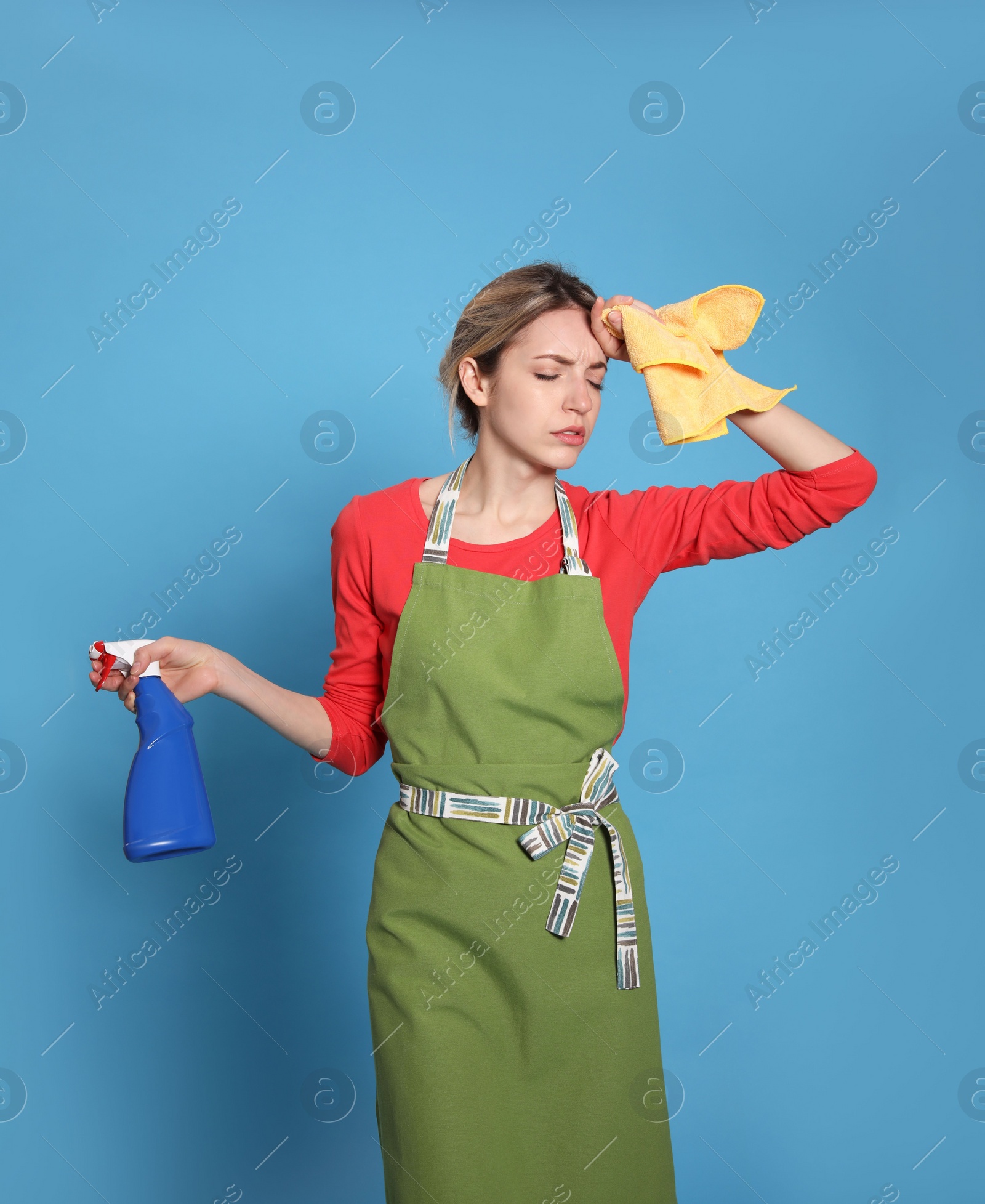 Photo of Young housewife with detergent and rag on light blue background