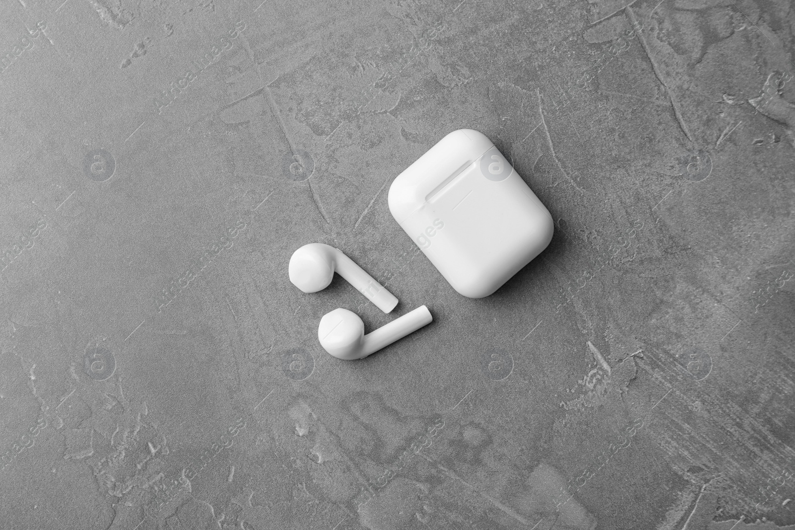 Photo of Wireless earphones and charging case on grey stone table, flat lay