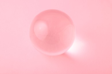 Photo of Transparent glass ball on light pink background