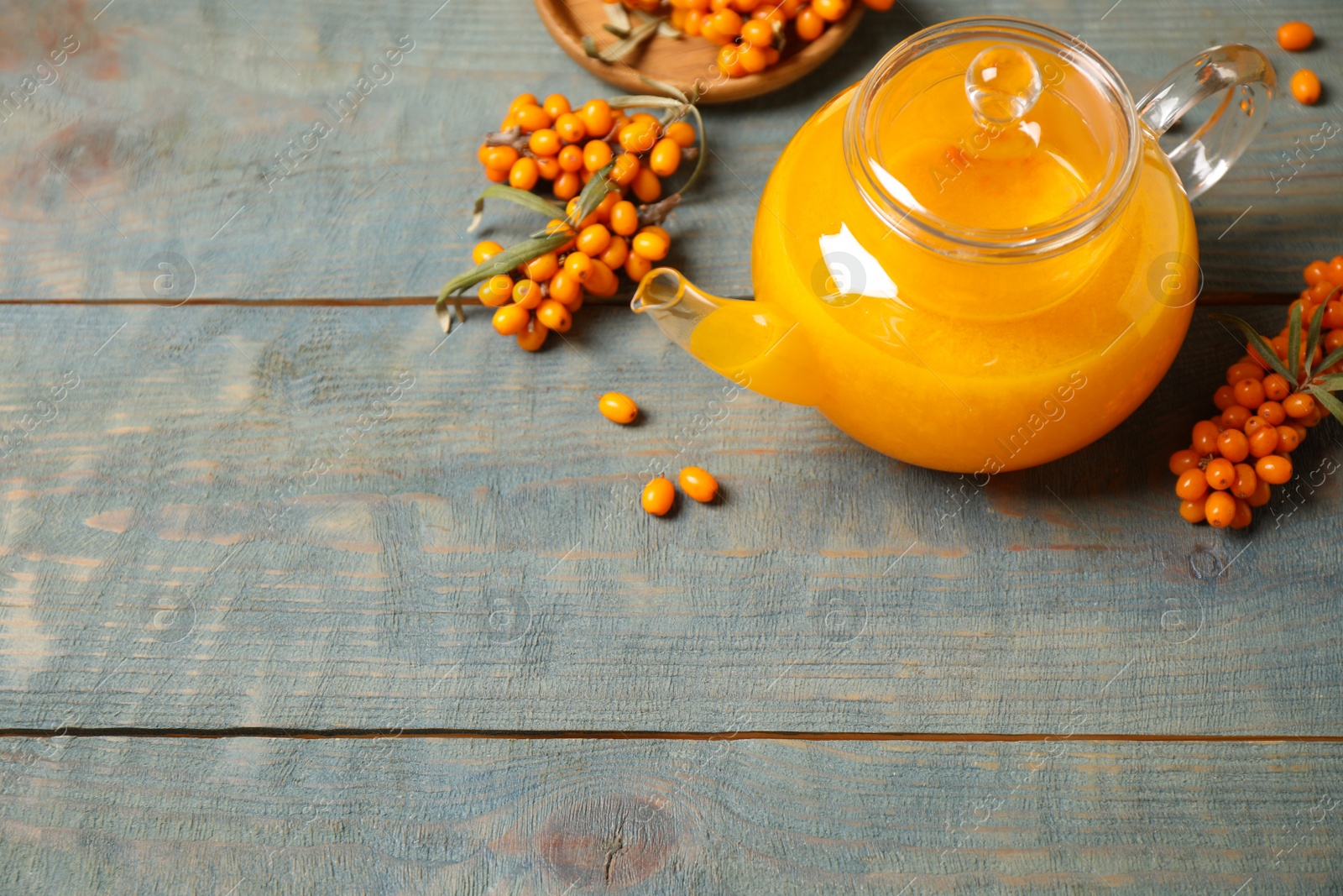 Photo of Delicious sea buckthorn tea and fresh berries on blue wooden table. Space for text