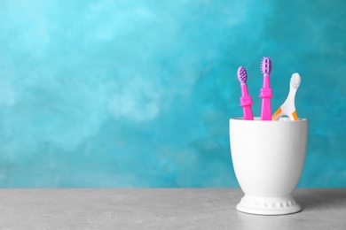 Baby toothbrushes in holder on table against color background with space for text