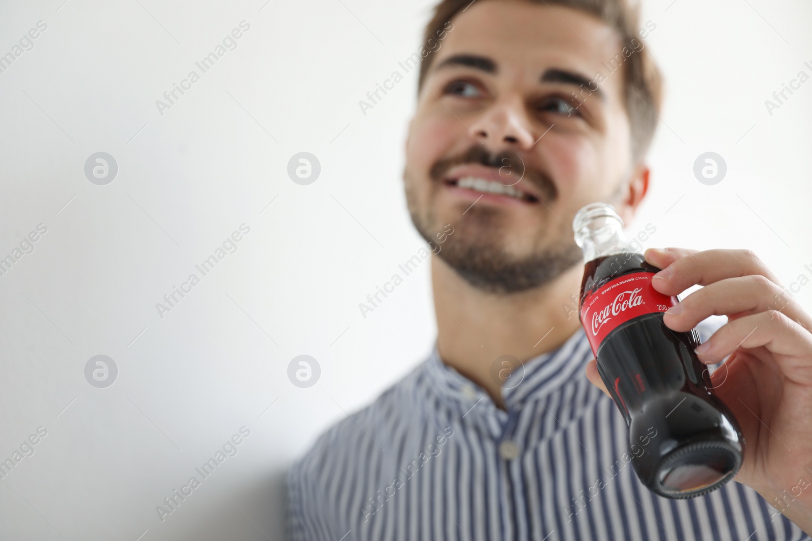 Photo of MYKOLAIV, UKRAINE - NOVEMBER 28, 2018: Young man with bottle of Coca-Cola on white background, closeup. Space for text