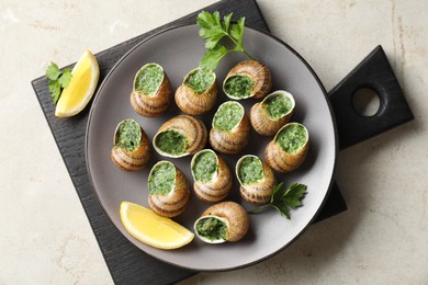 Photo of Delicious cooked snails with parsley and lemon on light table, top view