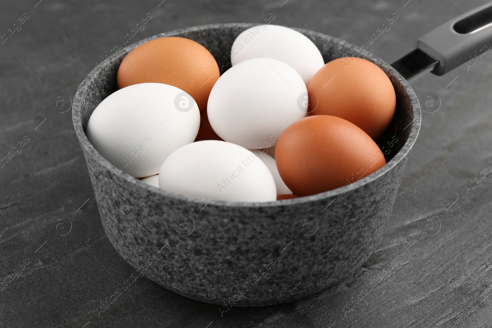 Photo of Unpeeled boiled eggs in saucepan on dark grey table, closeup