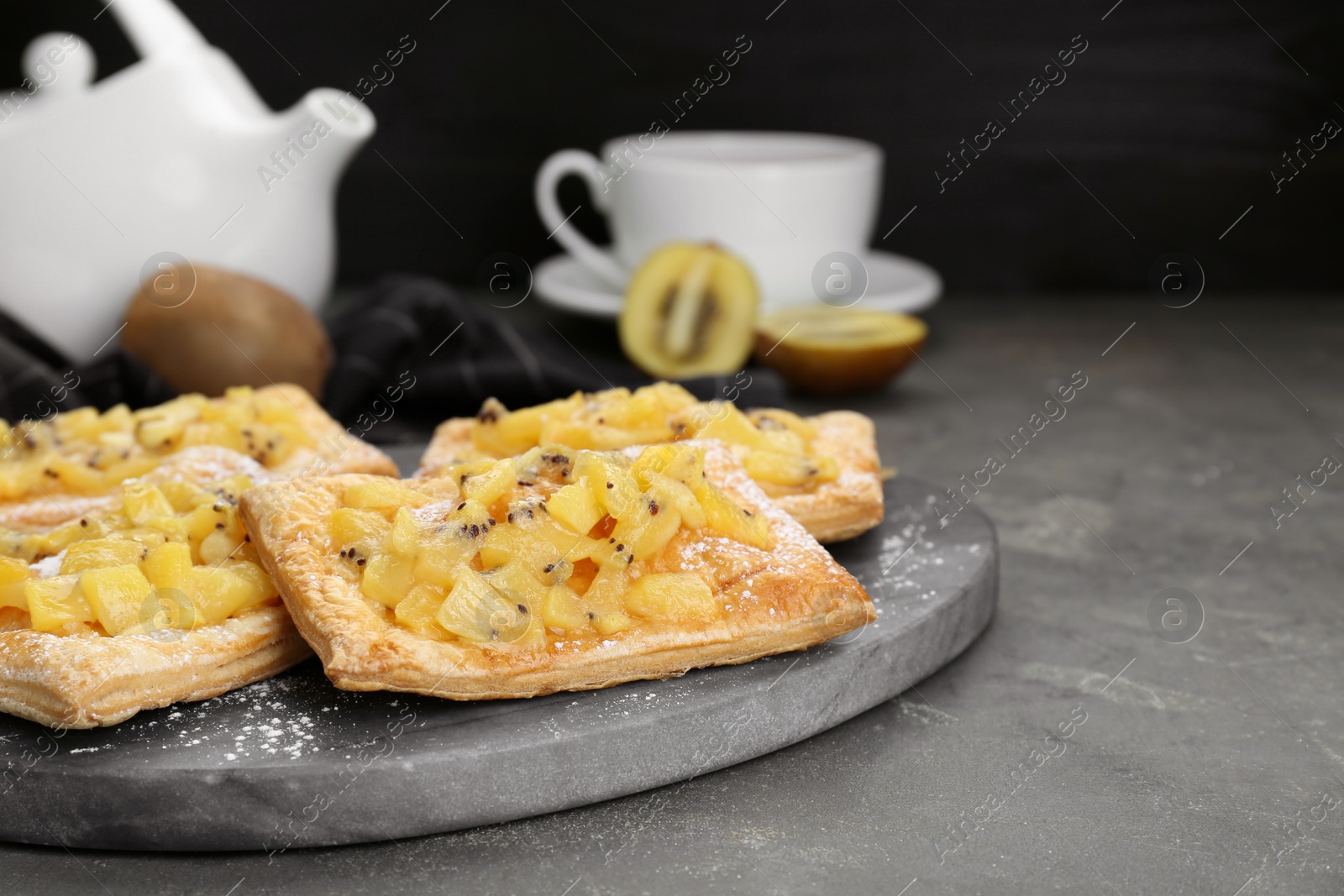Photo of Fresh tasty puff pastry with sugar powder and kiwi on grey table, closeup. Space for text