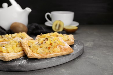 Photo of Fresh tasty puff pastry with sugar powder and kiwi on grey table, closeup. Space for text