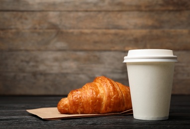 Photo of Paper cup with coffee and croissant on wooden table. Mockup for design
