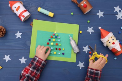 Photo of Little child making Christmas card at blue wooden table, top view