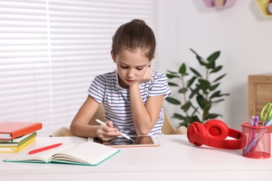 Photo of E-learning. Cute girl using tablet for studying online at table indoors