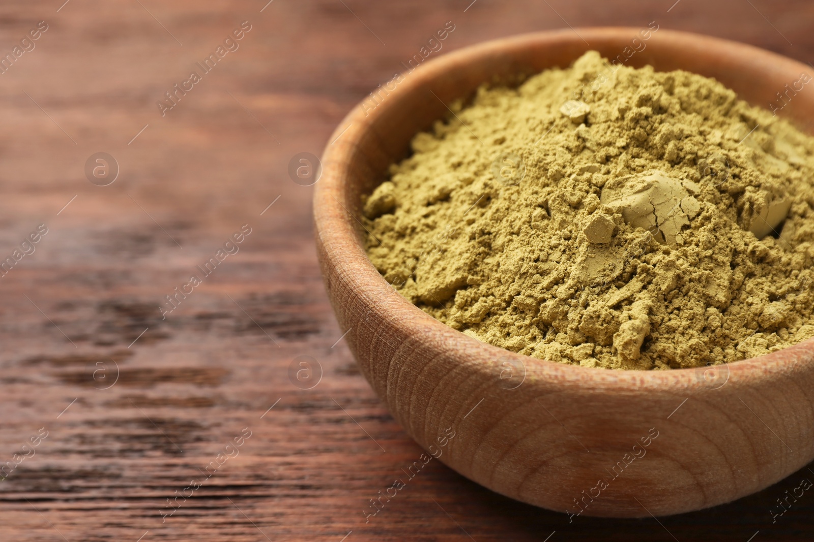 Photo of Bowl of henna powder on wooden table, closeup. Space for text