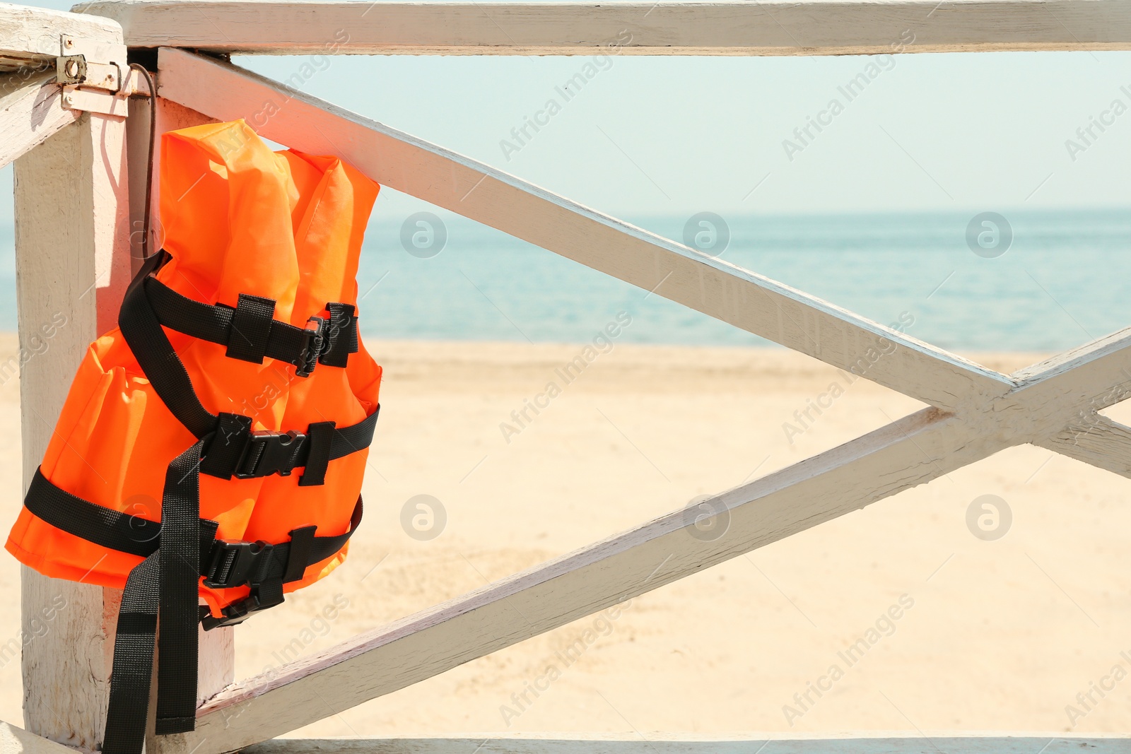 Photo of Orange life jacket hanging on wooden railing. Emergency rescue equipment