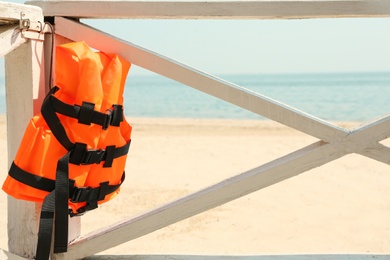 Photo of Orange life jacket hanging on wooden railing. Emergency rescue equipment