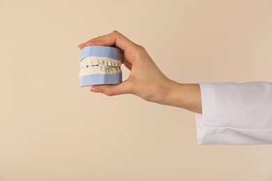 Doctor holding dental model with jaws on beige background, closeup. Cast of teeth