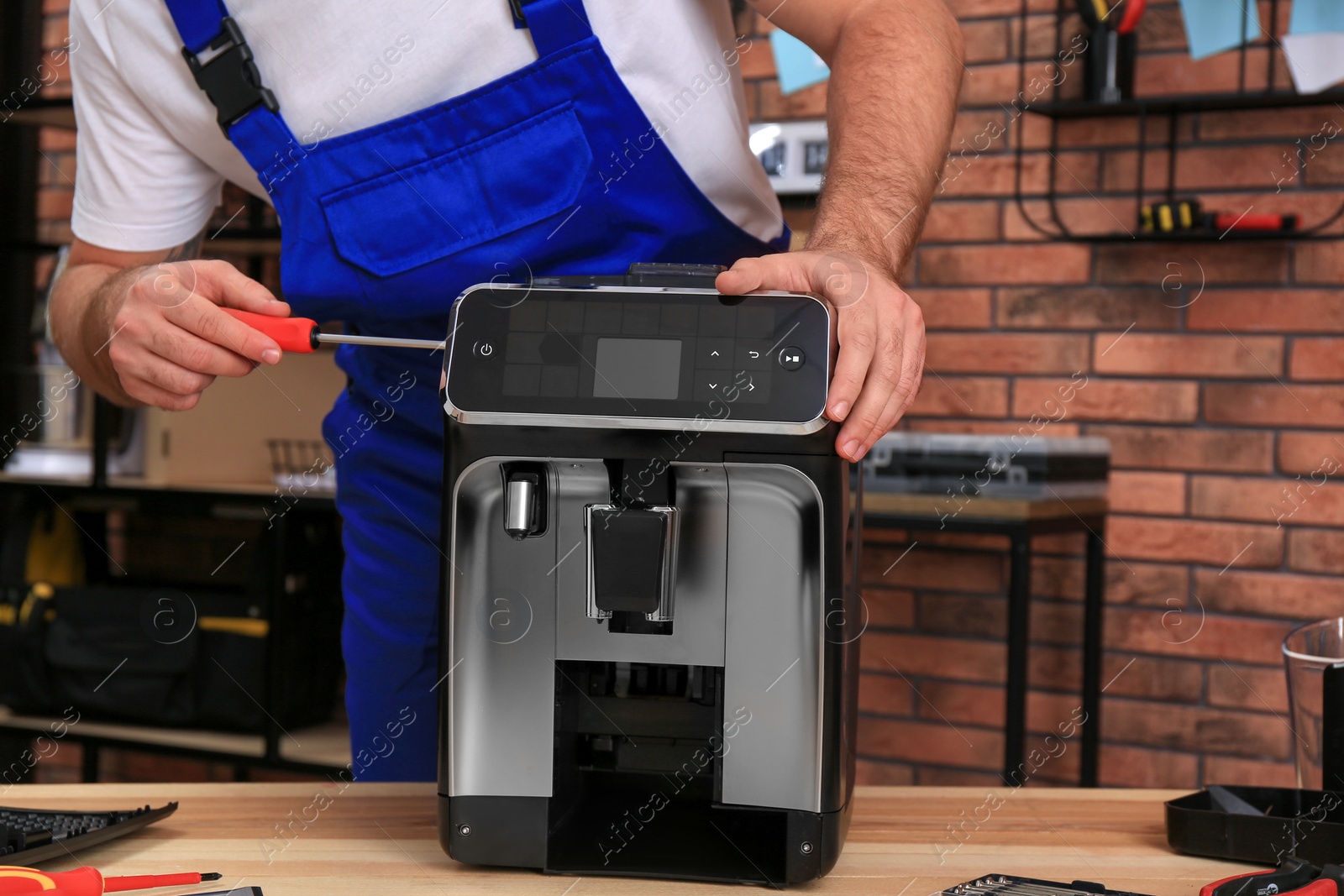 Photo of Repairman with screwdriver fixing coffee machine at table indoors, closeup