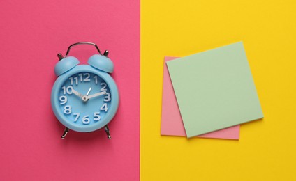 Alarm clock and blank reminder notes on color background, flat lay