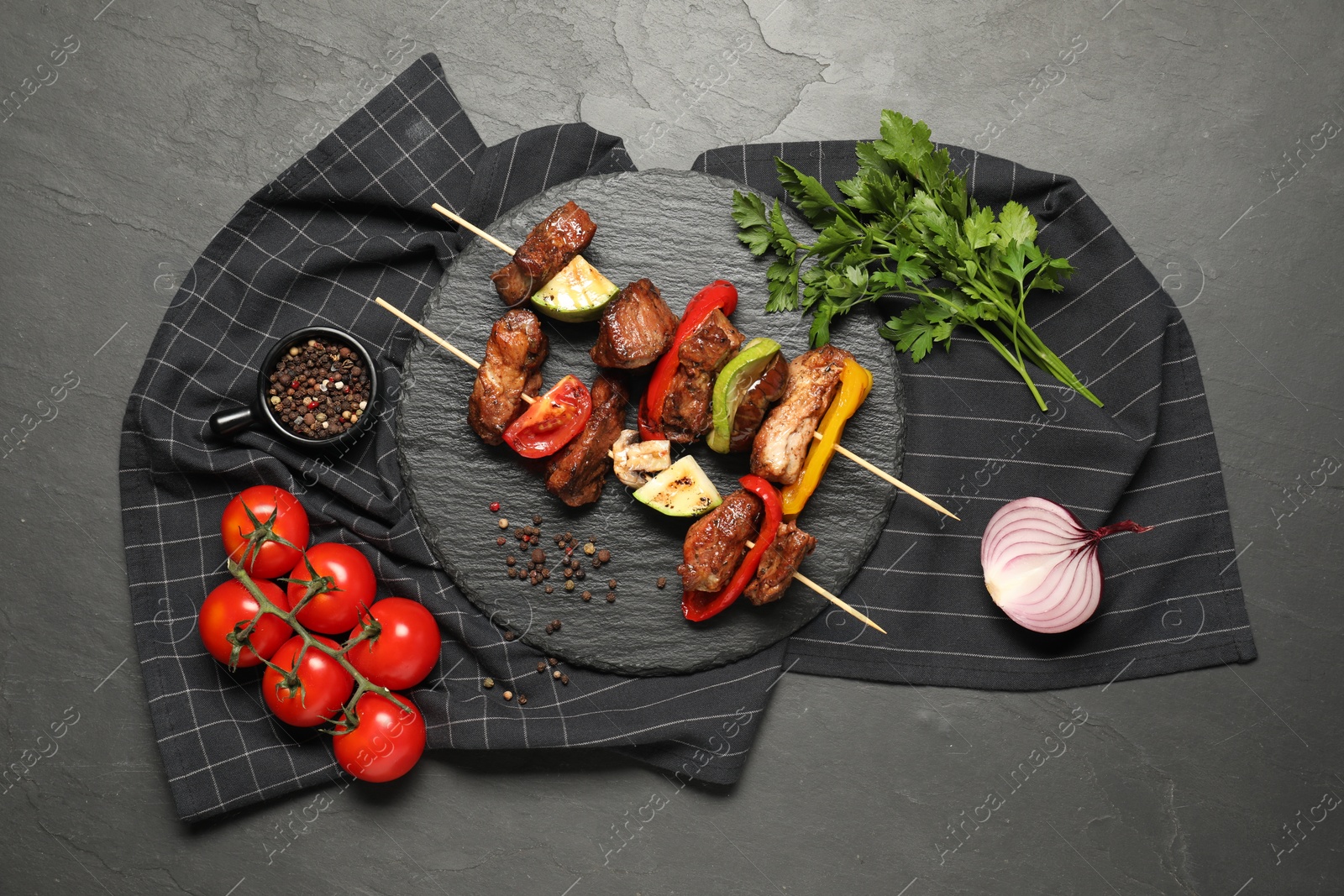 Photo of Delicious shish kebabs with vegetables and spices on grey textured table, flat lay