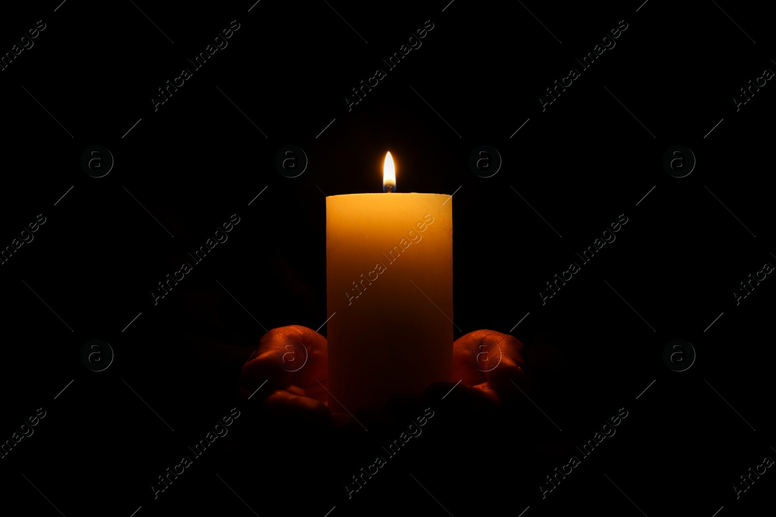 Photo of Woman holding burning candle in hands on black background, closeup