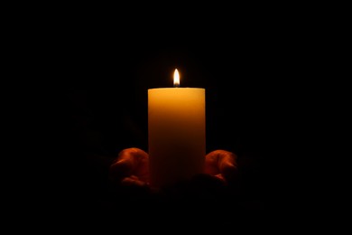 Photo of Woman holding burning candle in hands on black background, closeup