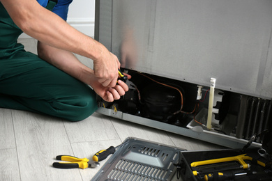 Photo of Male technician with pliers repairing refrigerator indoors, closeup