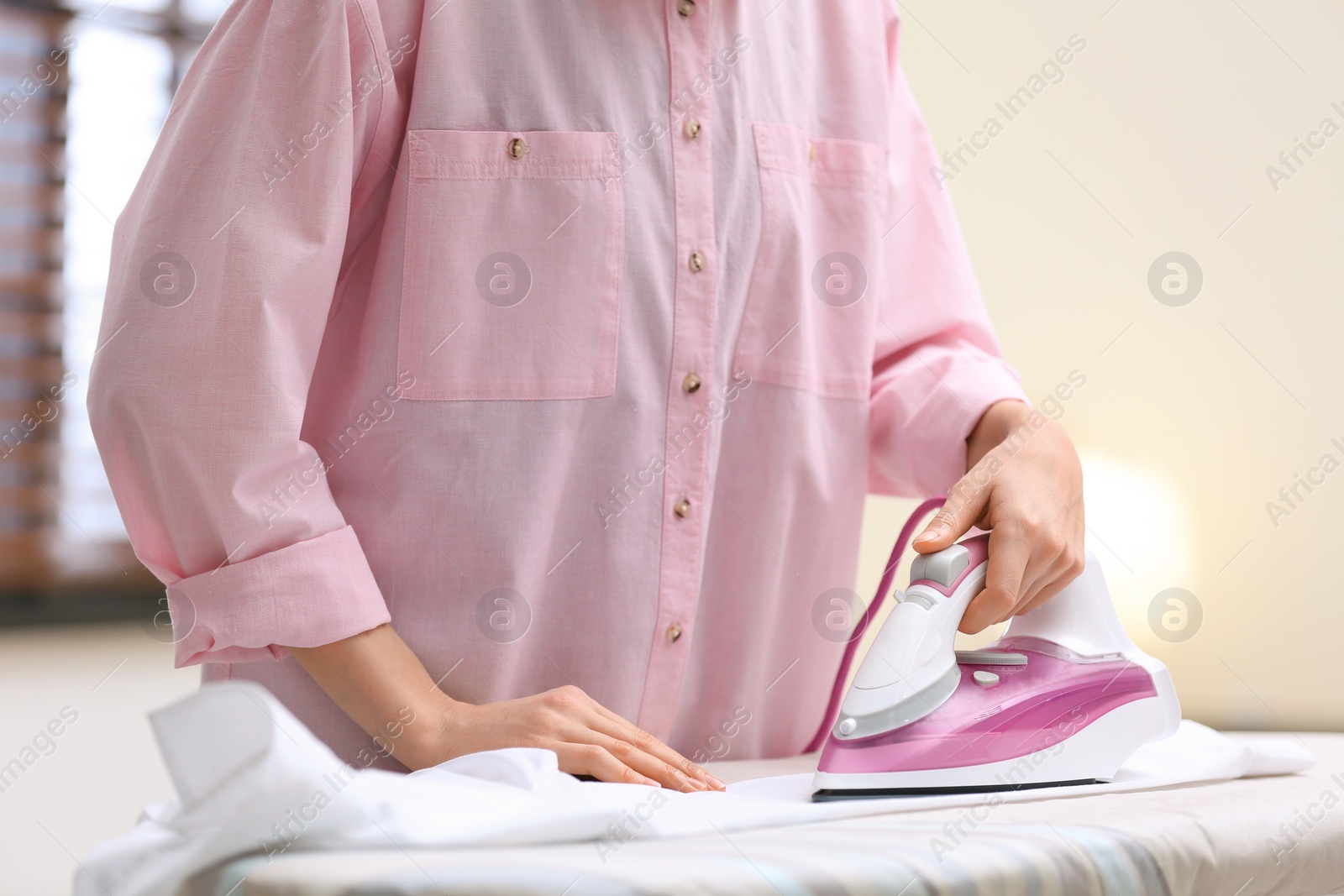 Photo of Woman ironing shirt on board indoors, closeup