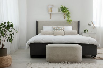 Stylish bedroom interior with large comfortable bed, ottoman and bedside table
