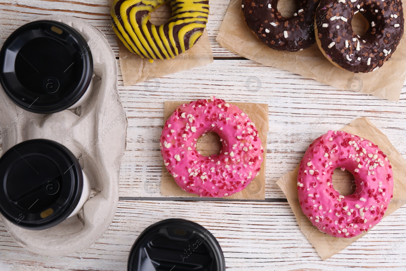 Photo of Tasty donuts and cups of hot drinks on white wooden table, flat lay