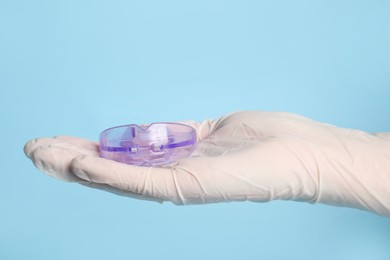 Photo of Dentist holding mouth guard on light blue background, closeup. Bite correction