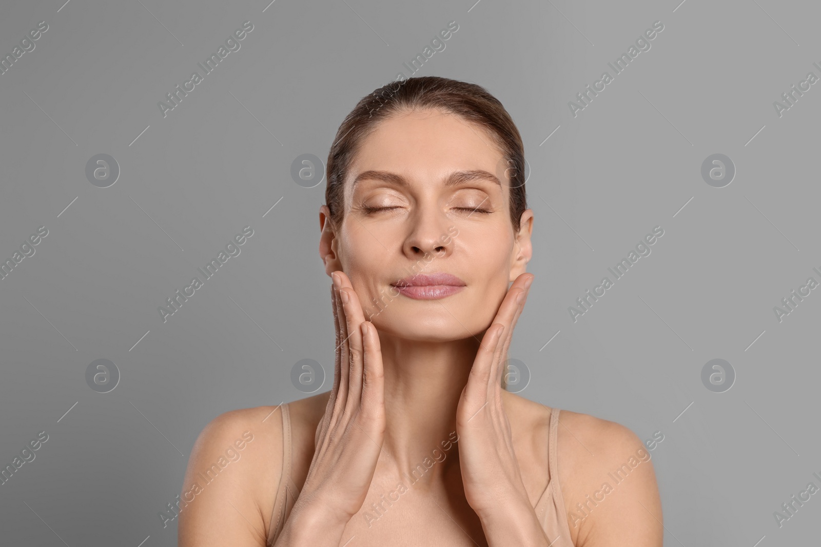 Photo of Woman massaging her face on grey background