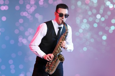 Image of Young man in elegant outfit playing saxophone on color background. Bokeh effect