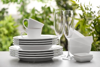 Photo of Set of clean dishware and champagne glasses on grey table against blurred background