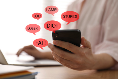 Image of Young woman holding smartphone at wooden table, closeup. Cyber bullying