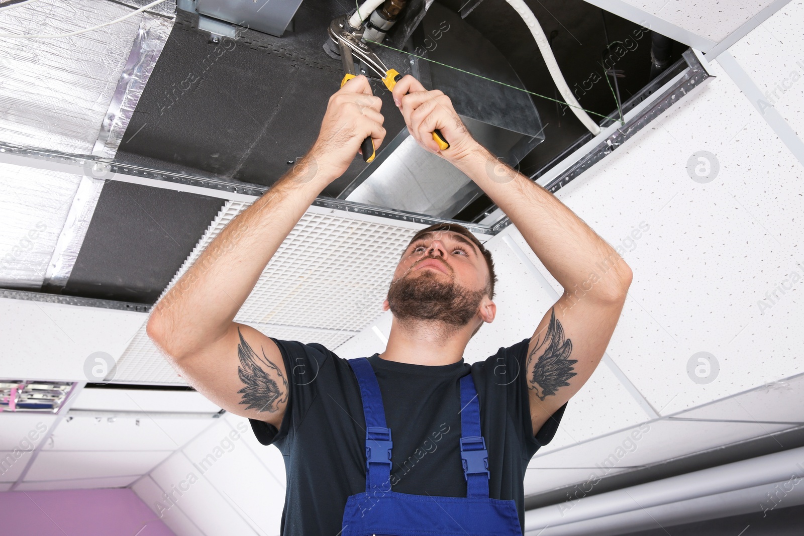 Photo of Young male technician repairing air conditioner indoors