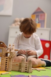 Little boy playing with wooden construction set on puzzle mat in room, selective focus. Child's toy