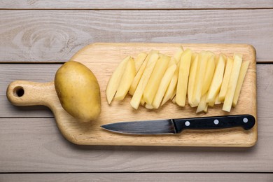 Whole and cut raw potatoes with knife on wooden table, top view