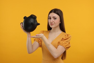 Sad woman with piggy bank on orange background