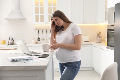 Photo of Tired pregnant woman working in kitchen at home. Maternity leave