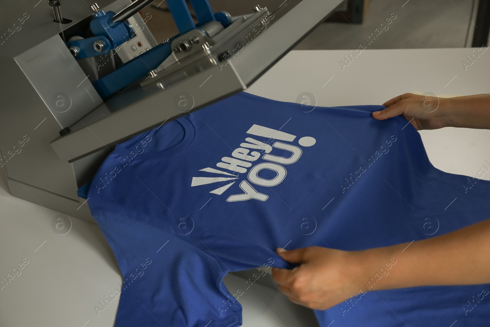 Photo of Printing logo. Woman with t-shirt using heat press at white table, closeup