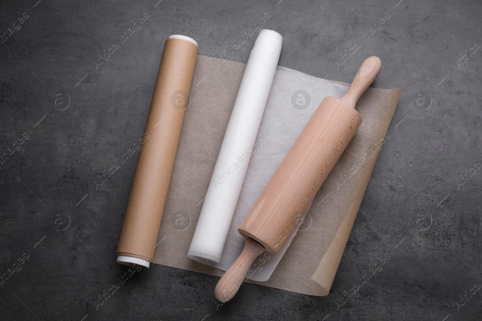 Photo of Rolls of baking paper and rolling pin on dark grey table, top view