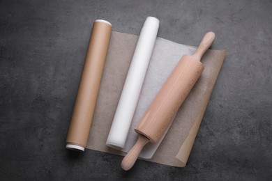 Rolls of baking paper and rolling pin on dark grey table, top view